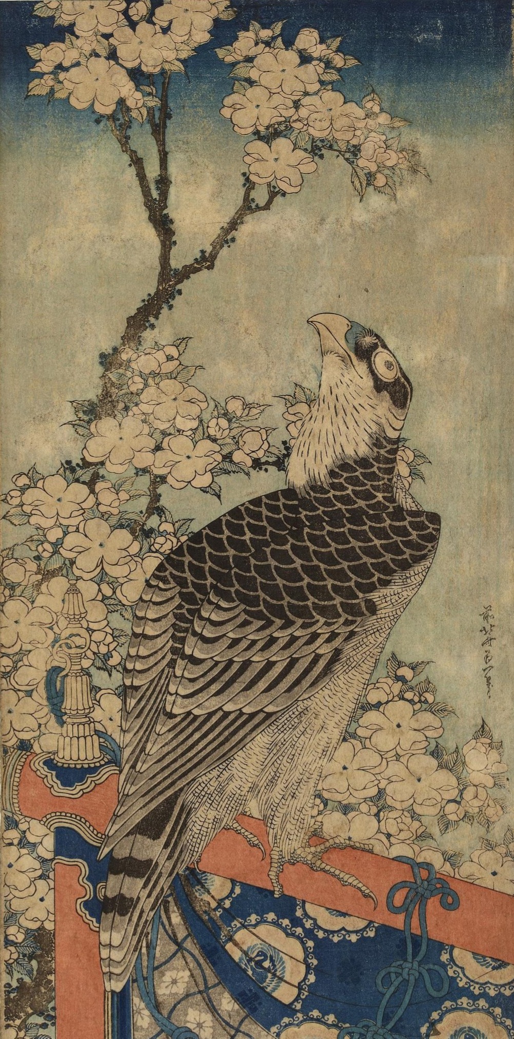 Bird of prey on an ornamental perch gazing at flowering cherry tree.